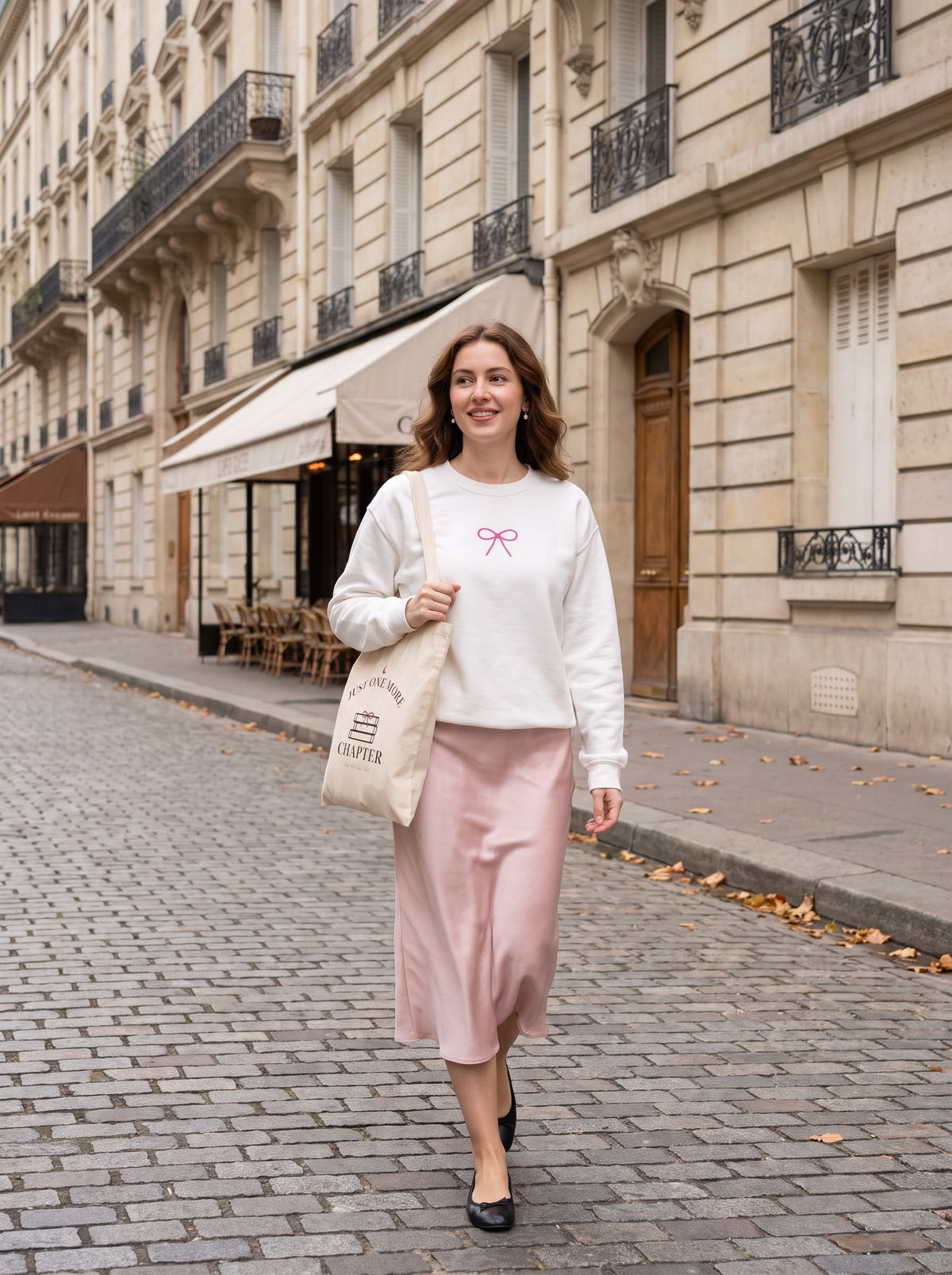 Woman on a Paris street wearing the white Coquette Bow embroidered crewneck with a pink satin skirt