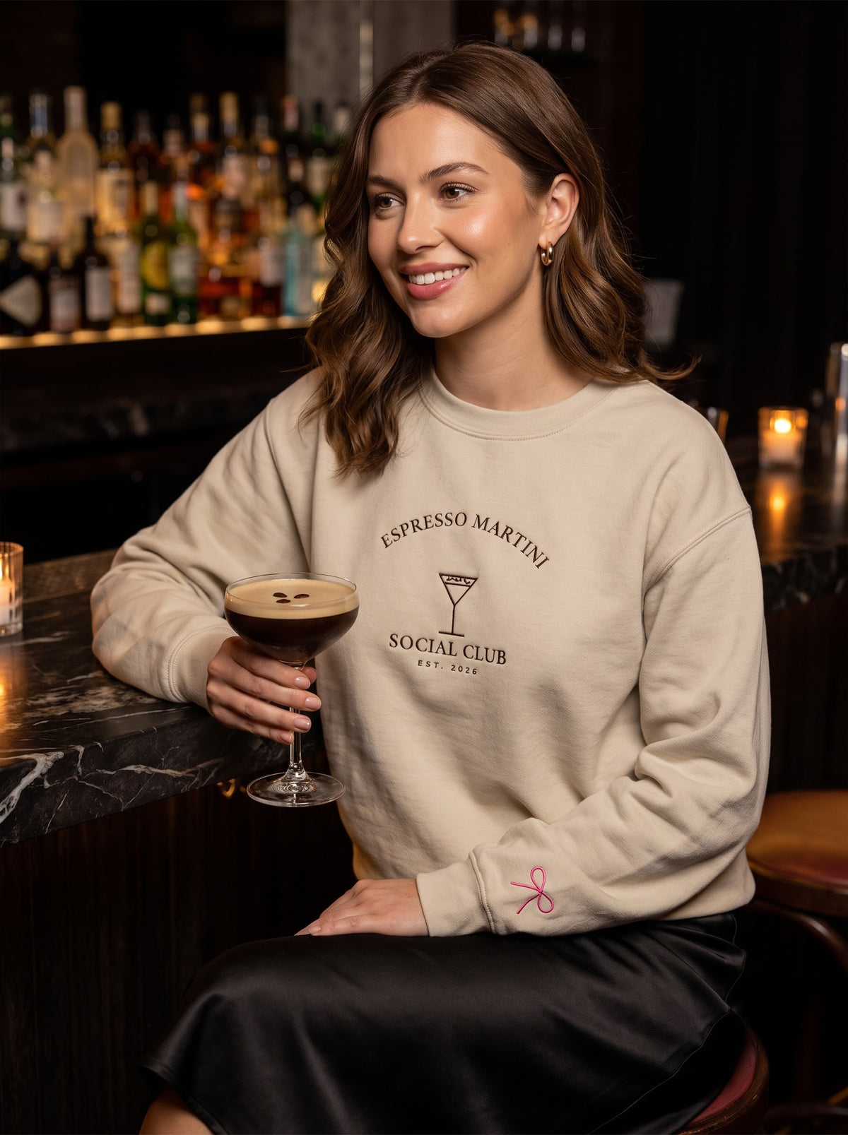Woman at a cocktail bar wearing the sand Espresso Martini Social Club embroidered crewneck