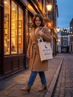 Woman walking past a bookshop at dusk carrying the Reading Under the Moon canvas tote