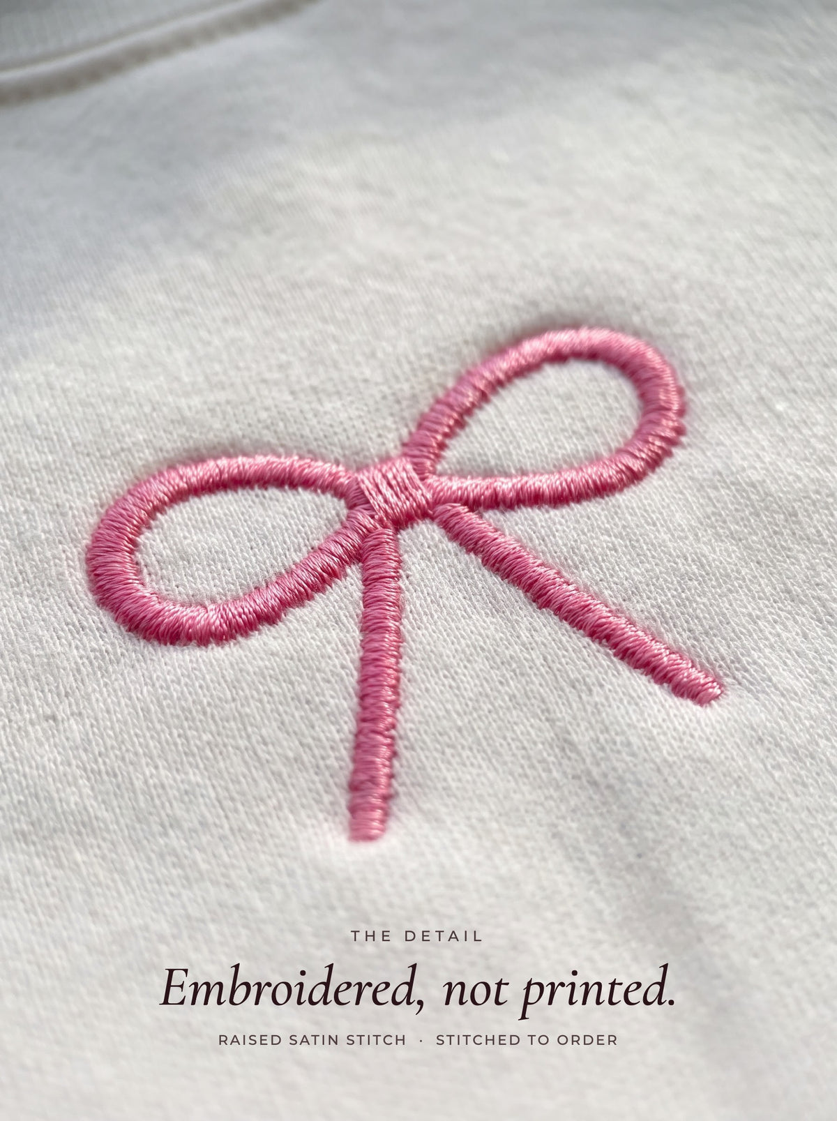 Close-up of the pink satin-stitch coquette bow embroidery on a white crewneck