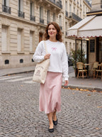 Woman walking a Paris street carrying the Just One More Chapter tote with a white bow sweatshirt and pink satin skirt
