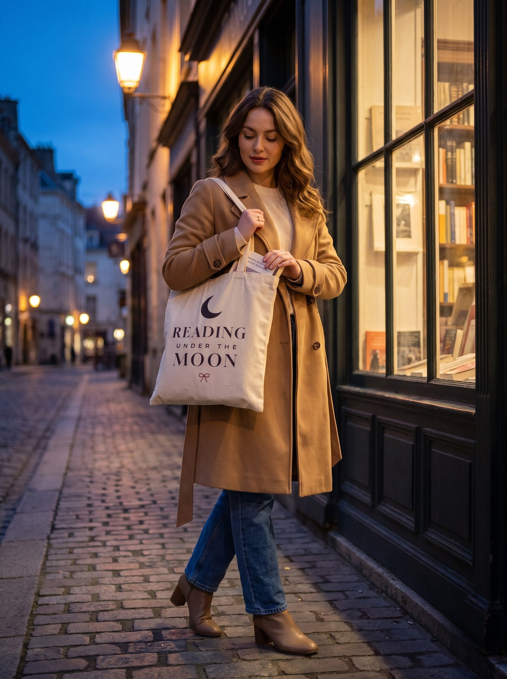 Woman in a camel coat reading a bookshop window display with the Reading Under the Moon tote