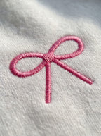 Macro of the raised pink bow embroidery with visible satin-stitch threads on a white sweatshirt