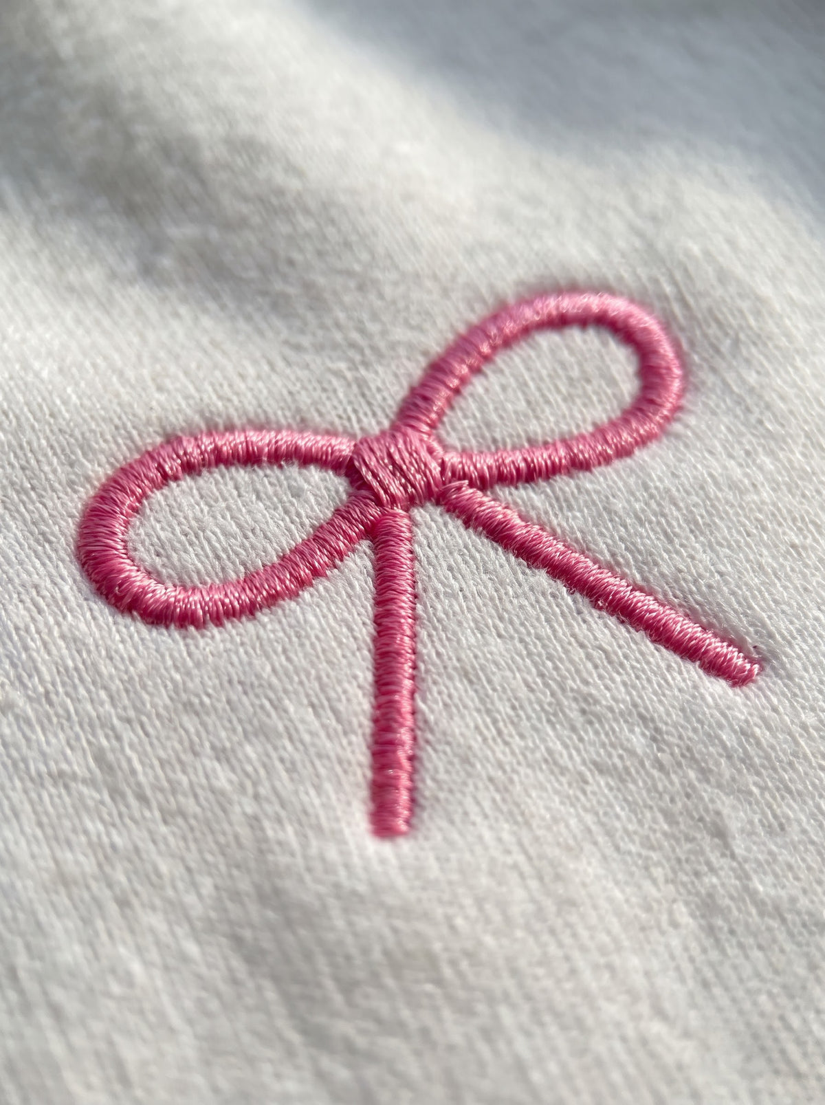 Macro of the raised pink bow embroidery with visible satin-stitch threads on a white sweatshirt