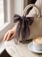 Plum tartan scarf with crescent moons tied to a handbag handle on a marble café table