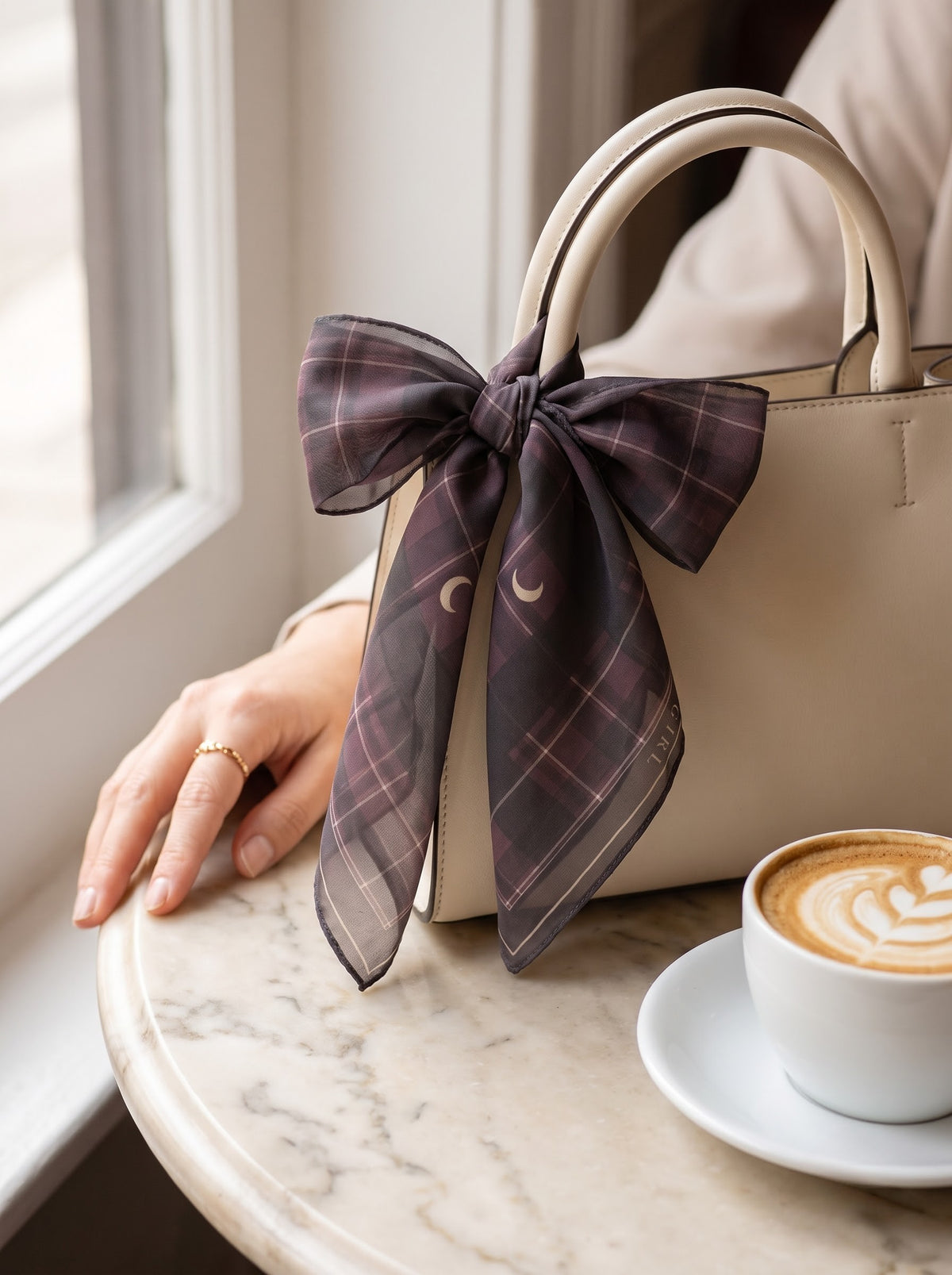 Plum tartan scarf with crescent moons tied to a handbag handle on a marble café table