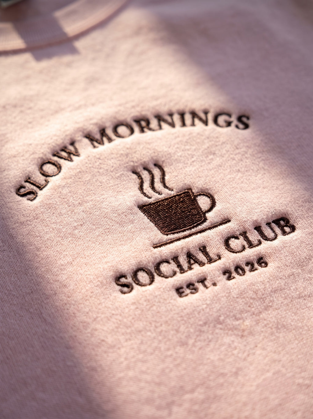 Macro of the raised satin-stitch coffee cup and lettering on the Slow Mornings Social Club crewneck