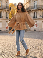 Model spinning on a Paris cobblestone street so the camel cape sleeves and tie belt of the City Muse coat swing out