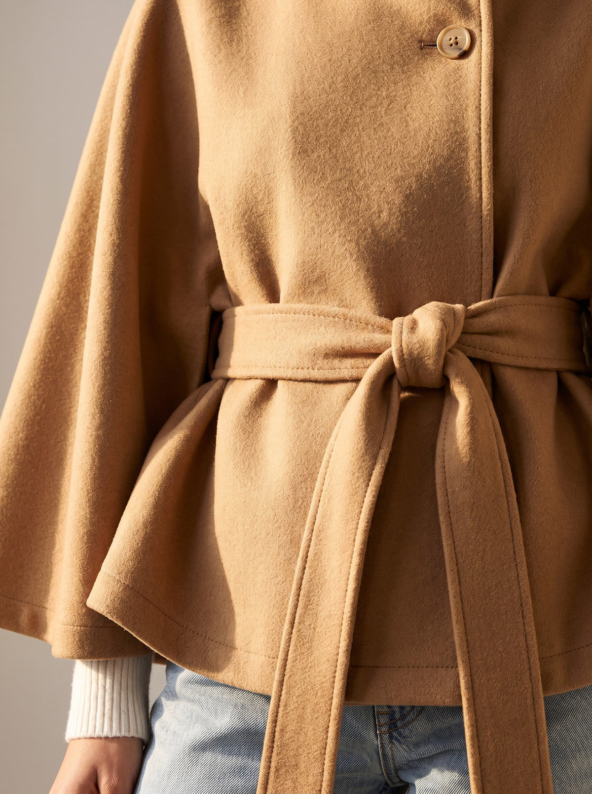 Detail of the camel City Muse cape coat fabric texture, button and knotted tie belt