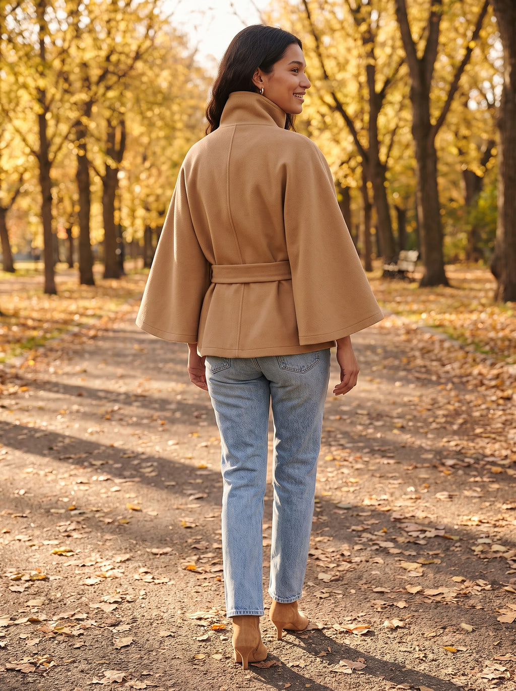 Back view of the camel City Muse cape coat with tie belt, worn on an autumn park path