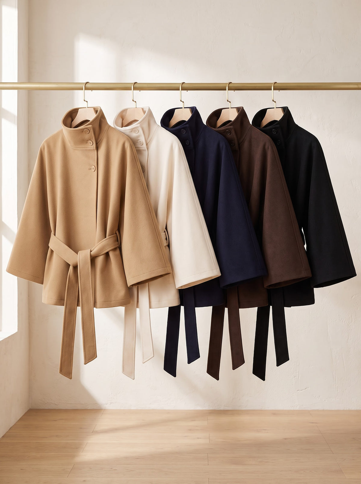 City Muse belted cape coat in all five colors on a rail: camel, cream, navy, chocolate and black