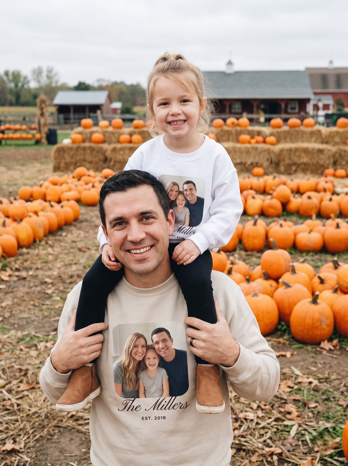 Dad in a sand custom photo sweatshirt carrying his daughter in a white kids photo crewneck at a pumpkin patch