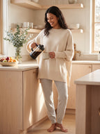 Woman pouring coffee in a sunny kitchen wearing the cream oversized batwing sweater with lounge pants