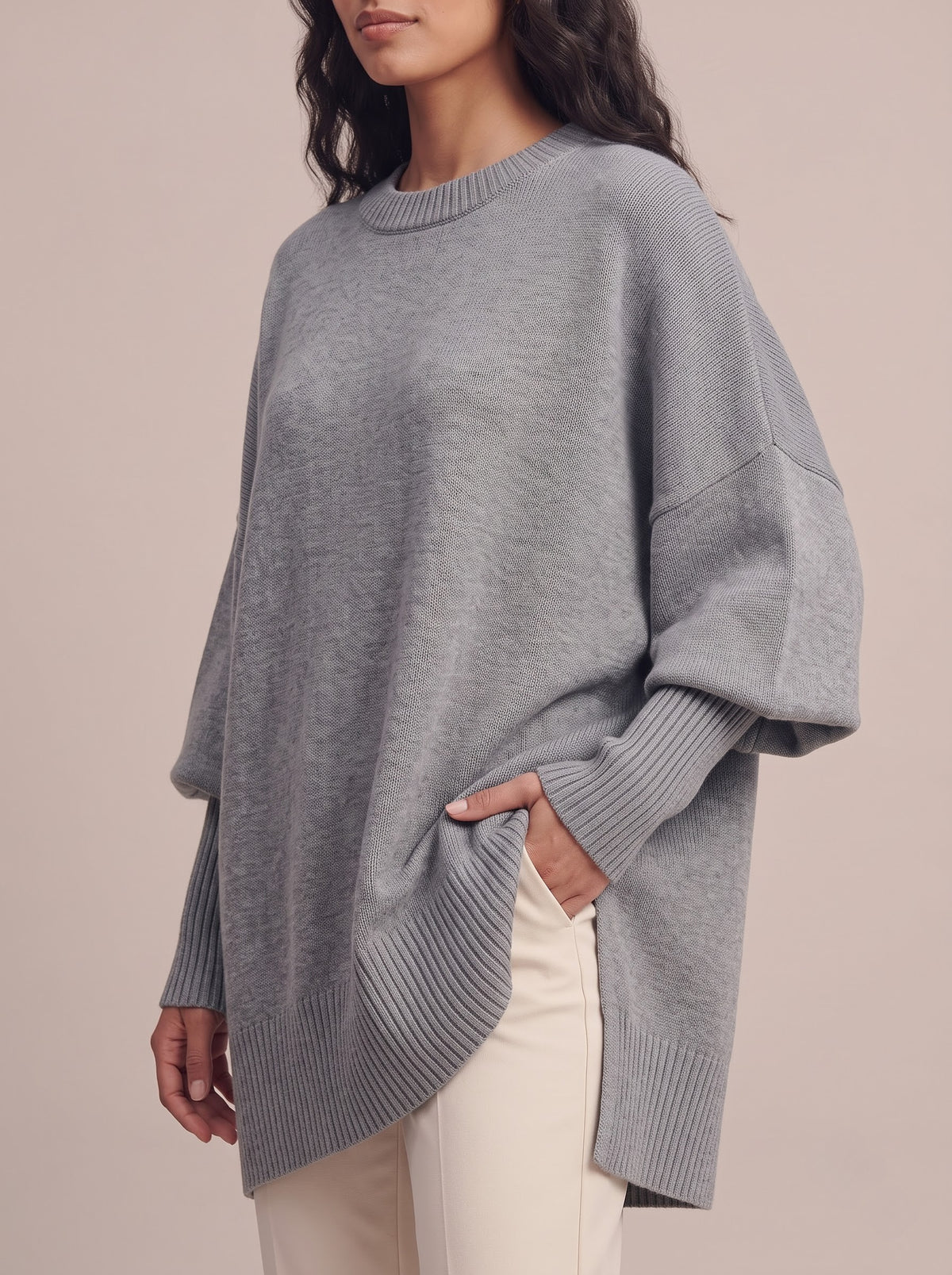 Close-up of the gray oversized sweater showing the batwing sleeve, long ribbed cuff and ribbed high-low hem with side slit