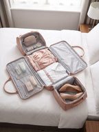 Pink Getaway garment duffle bag unzipped and opened flat on a hotel bed, packed with a dress, shirt and heels