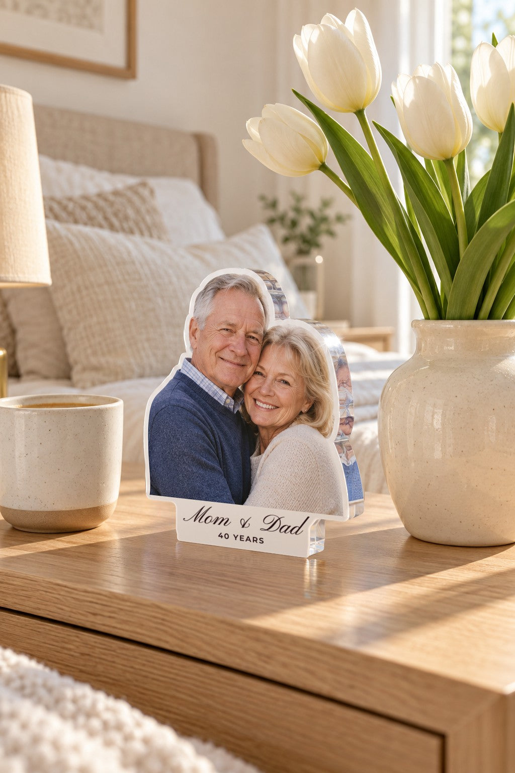 Clear acrylic photo block of a smiling older couple, white tab reading Mom & Dad and 40 YEARS, on an oak bedside table by tulips