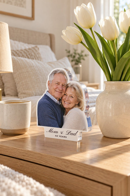 Clear acrylic photo block of a smiling older couple, white tab reading Mom & Dad and 40 YEARS, on an oak bedside table by tulips