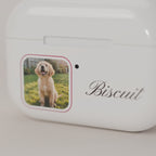 Close-up of the personalized AirPods case print: golden retriever photo in a rose-traced window and Biscuit in script on a glossy cream shell