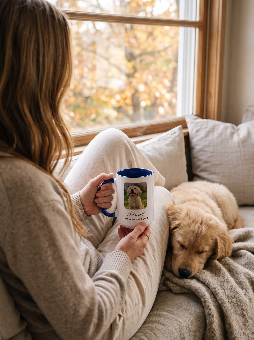 Mom holding a custom pet photo mug on a window seat while her golden retriever puppy naps beside her