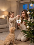 Mom and daughter hanging a custom heart photo ornament on the Christmas tree with their puppy