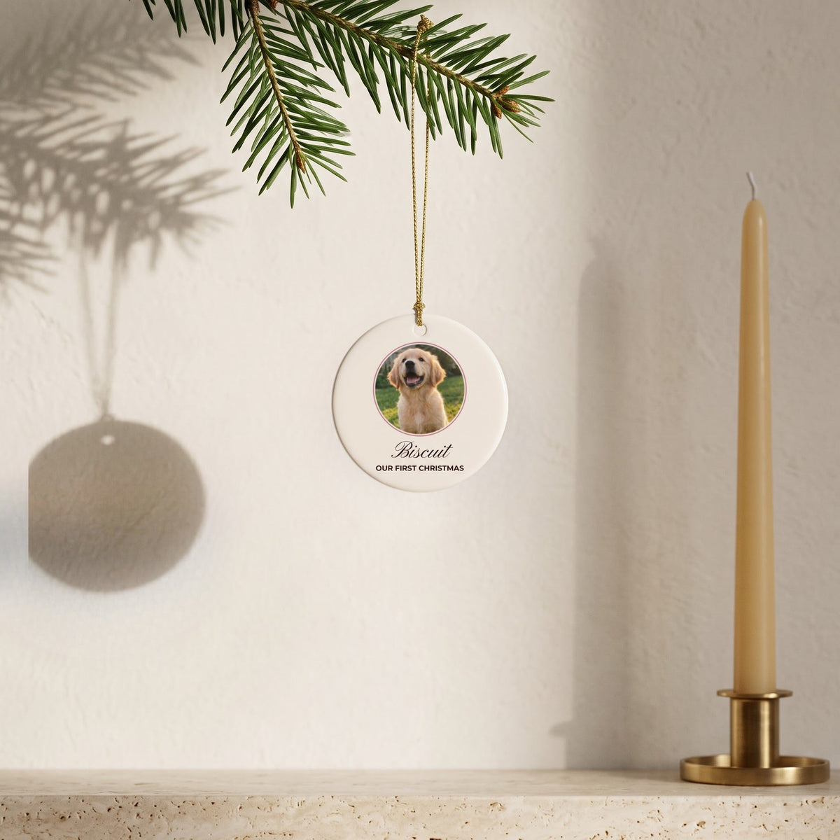 Round custom puppy photo ornament hanging from a fir sprig beside a candle