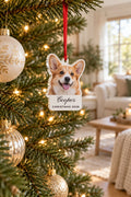 Acrylic corgi photo ornament with a white name tab printed Cooper and CHRISTMAS 2026, hung by a red ribbon on a lit Christmas tree
