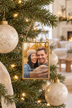 Gold-edged glass frame ornament with a couple selfie, Emma & James and Our First Christmas, on a gold chain on a lit Christmas tree