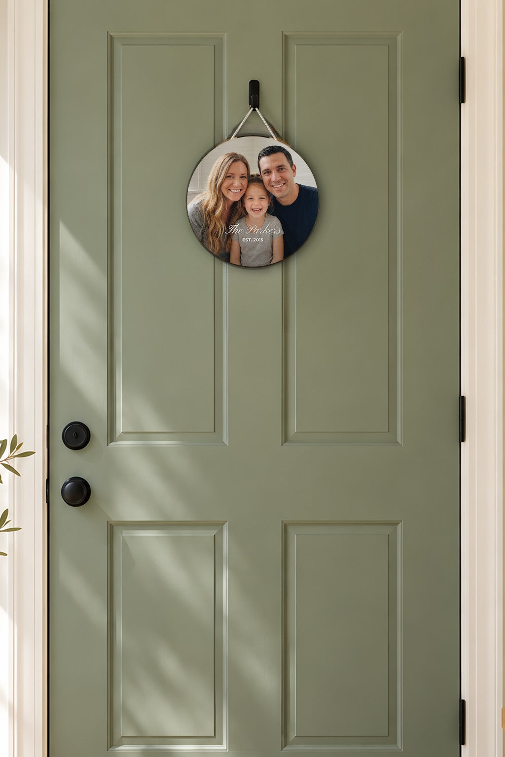 Round wood sign printed with a family photo, The Parkers and Est. 2015, hung by a cream cord on a sage front door