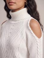 Close-up of the white turtleneck sweater showing the ribbed collar, cold-shoulder cut-out, cable-knit sleeve and pointelle knit texture