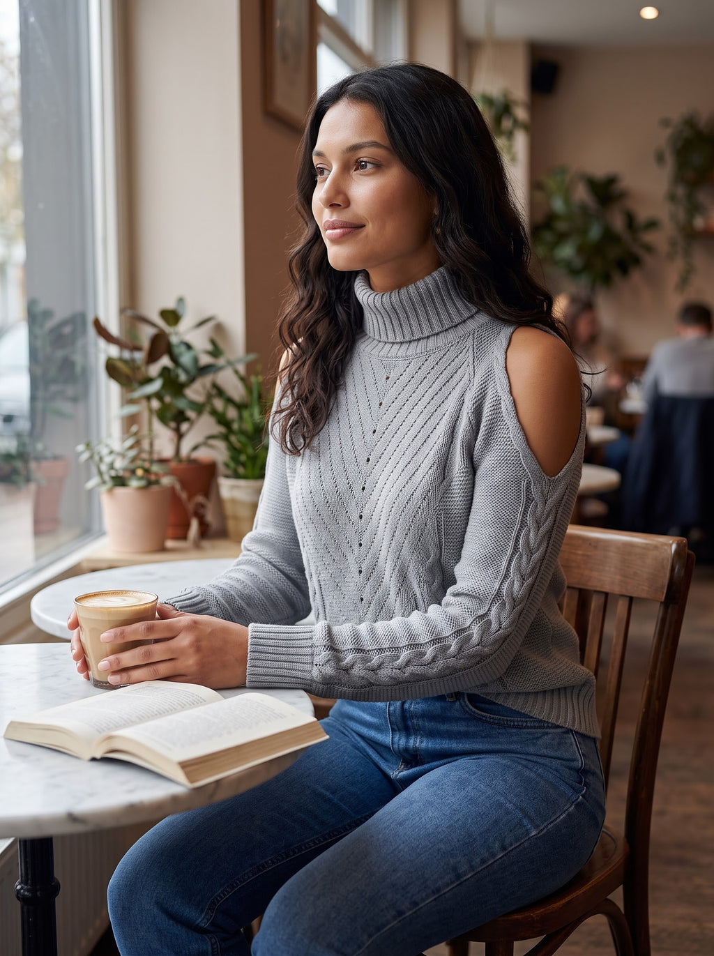Gray cold-shoulder turtleneck knit sweater styled with jeans at a cafe table with a latte and a book
