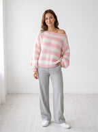Weekend Stripe off-shoulder knit sweater in pink and cream wide stripes, worn with gray wide-leg trousers, studio photo