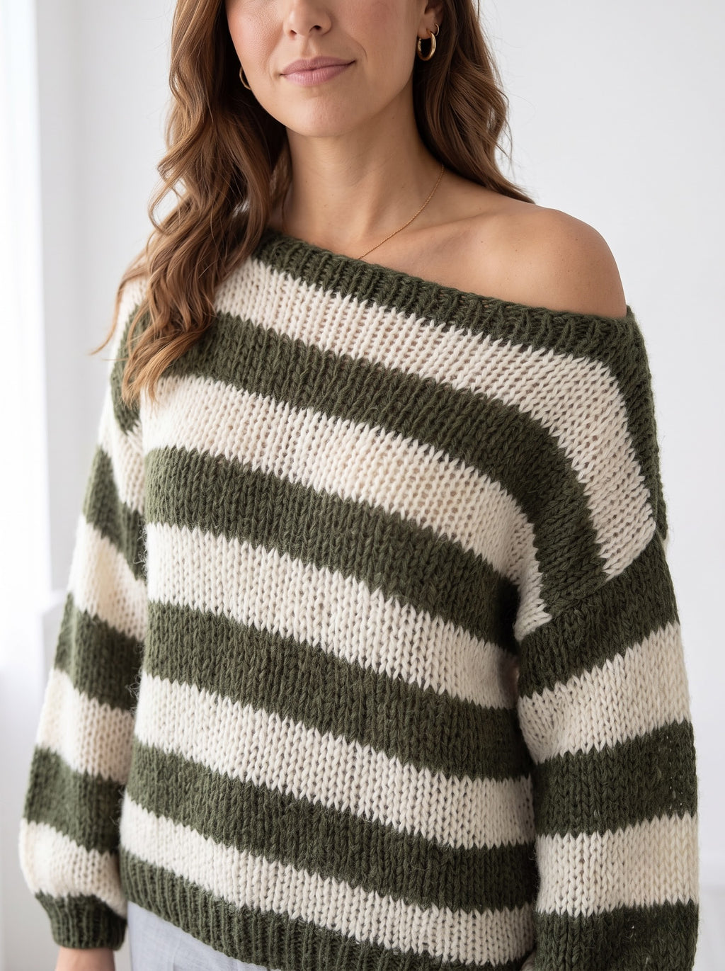 Close-up of the loose-gauge open knit and wide boat neckline worn off the shoulder, military green stripes