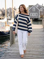 Woman walking on a harbor dock in the navy and cream striped off-shoulder sweater with white jeans and a canvas tote