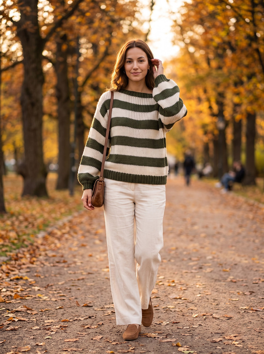 Woman walking in an autumn park in the military green and cream striped knit sweater with cream trousers